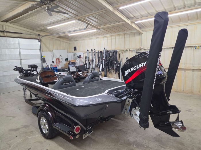 A bass boat on its trailer, seen from the stern, inside the K5 shop, with trolling motors and shallow water anchors lined up along the back wall